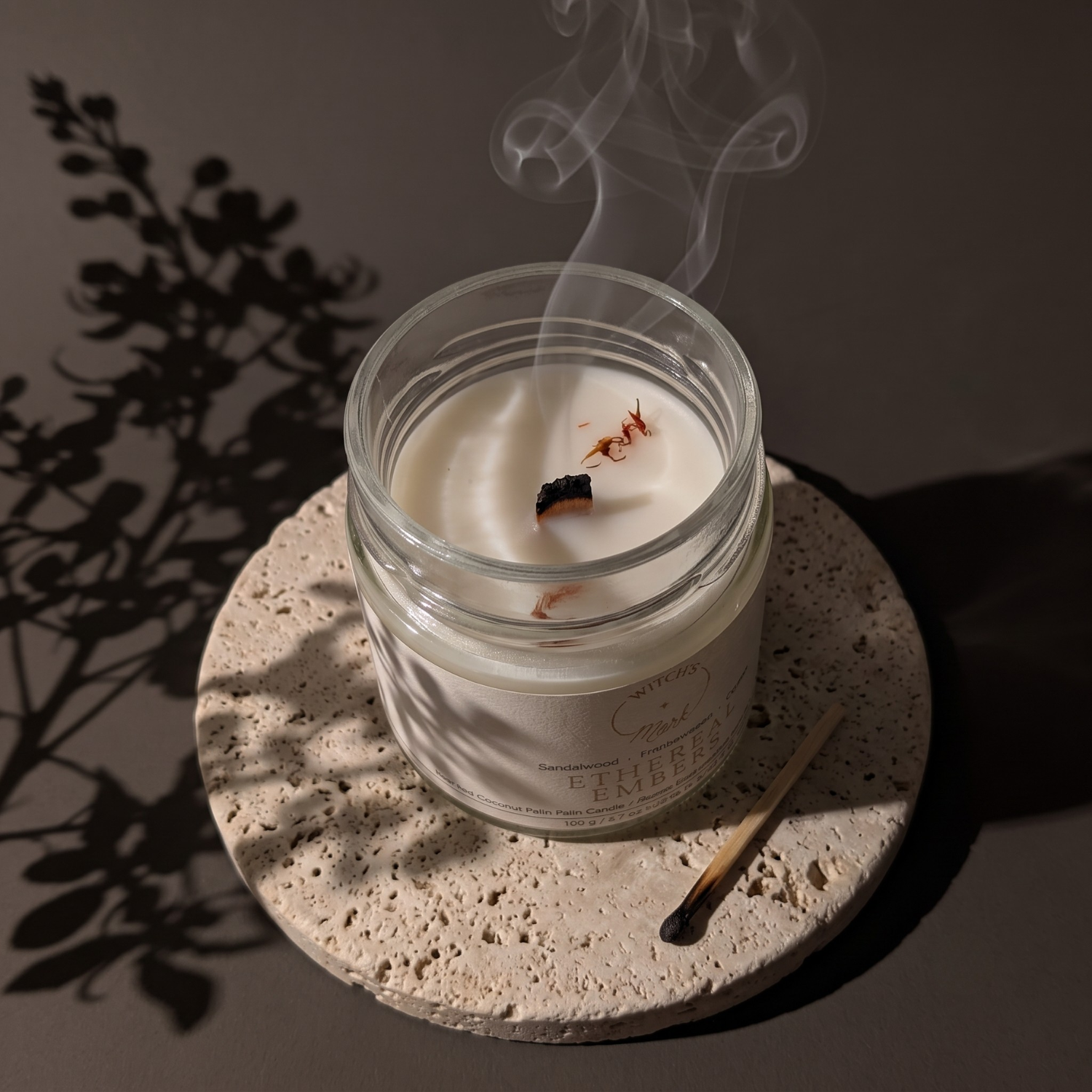 Ethereal Embers crystal candle extinguished with smoke dancing up from the unlit wick. The candle is on a coaster and next to the coaster is a burnt match.