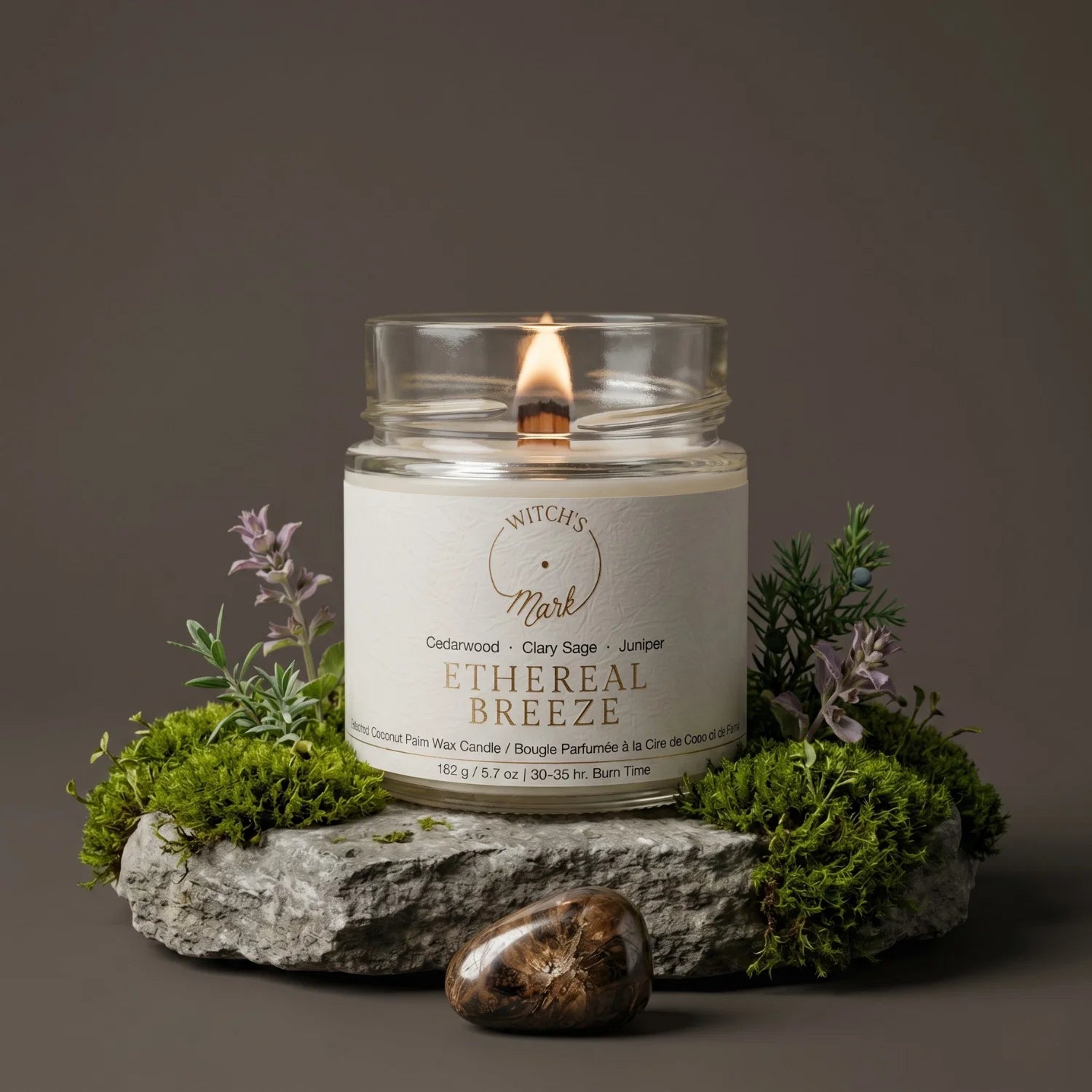 Ethereal Breeze candle on a rock surrounded by a bed of moss, clary sage & juniper. In front of the candle is a bronzite crystal.