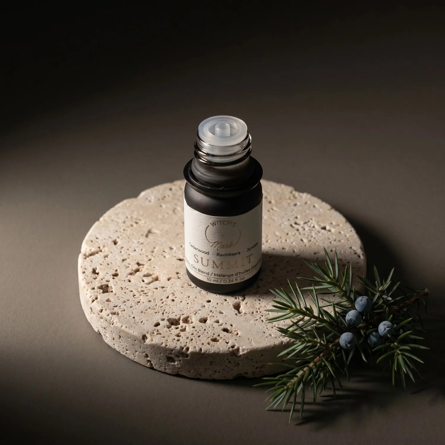 Summit essential oil bottle on a porous stone coaster with a sprig of juniper next to the coaster.