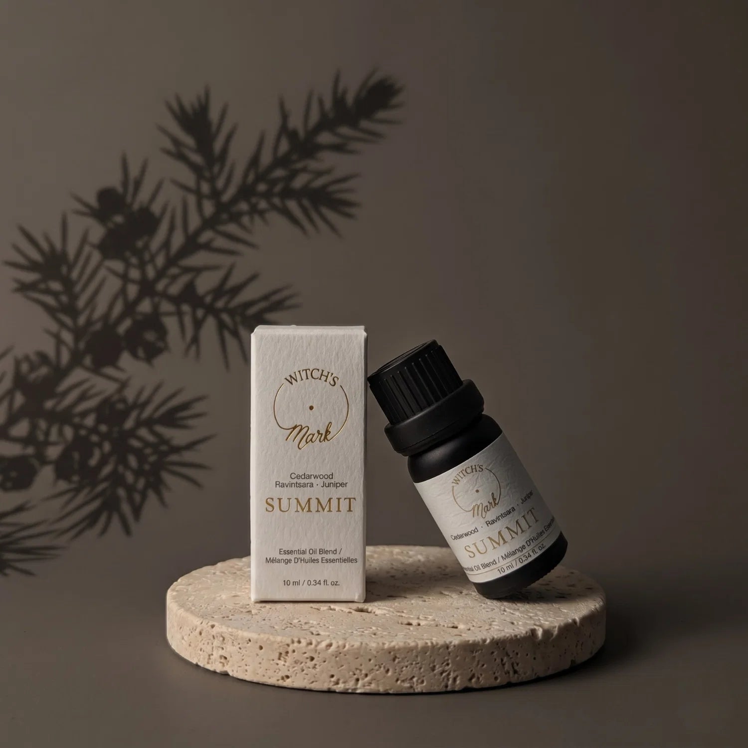 Summit essential oil bottle with packaging on a porous stone coaster. In the background is a shadow of a juniper branch.