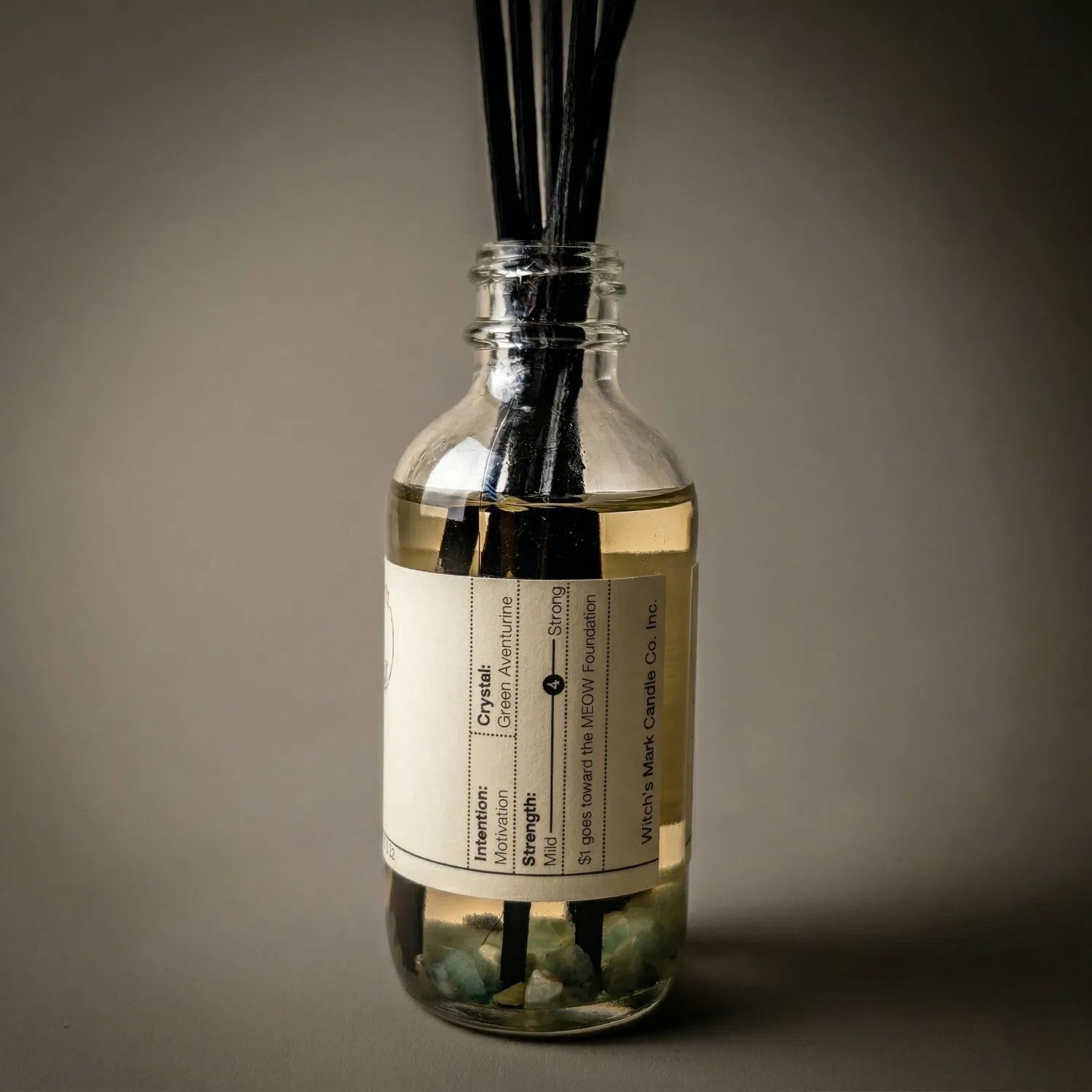 A warmly lit close-up of the Waxing Moon spell jar reed diffuser, revealing the empowering green aventurine crystals submerged at the bottom of the golden botanical oil, crafted to invoke success and fierce confidence.