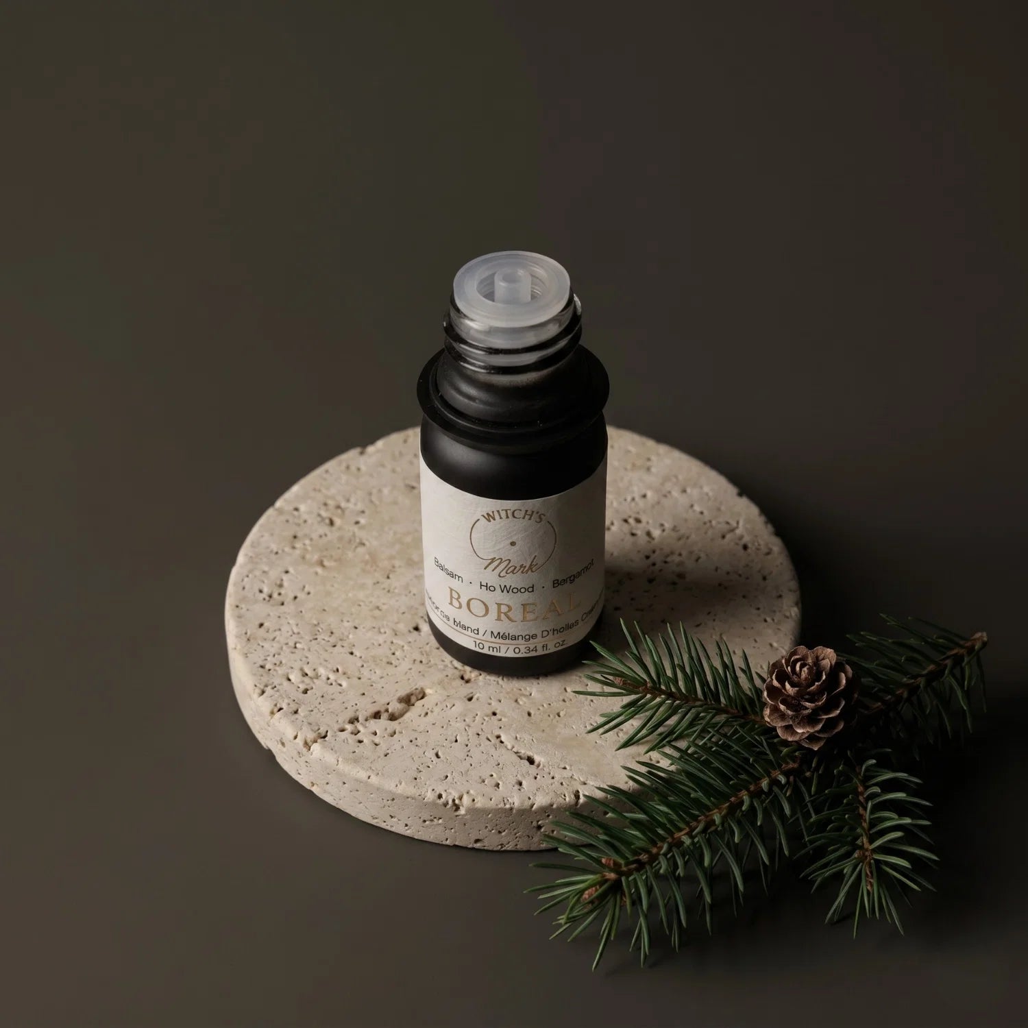 Bottle of Borea essential oil on a stone coaster with pine branches and cones.