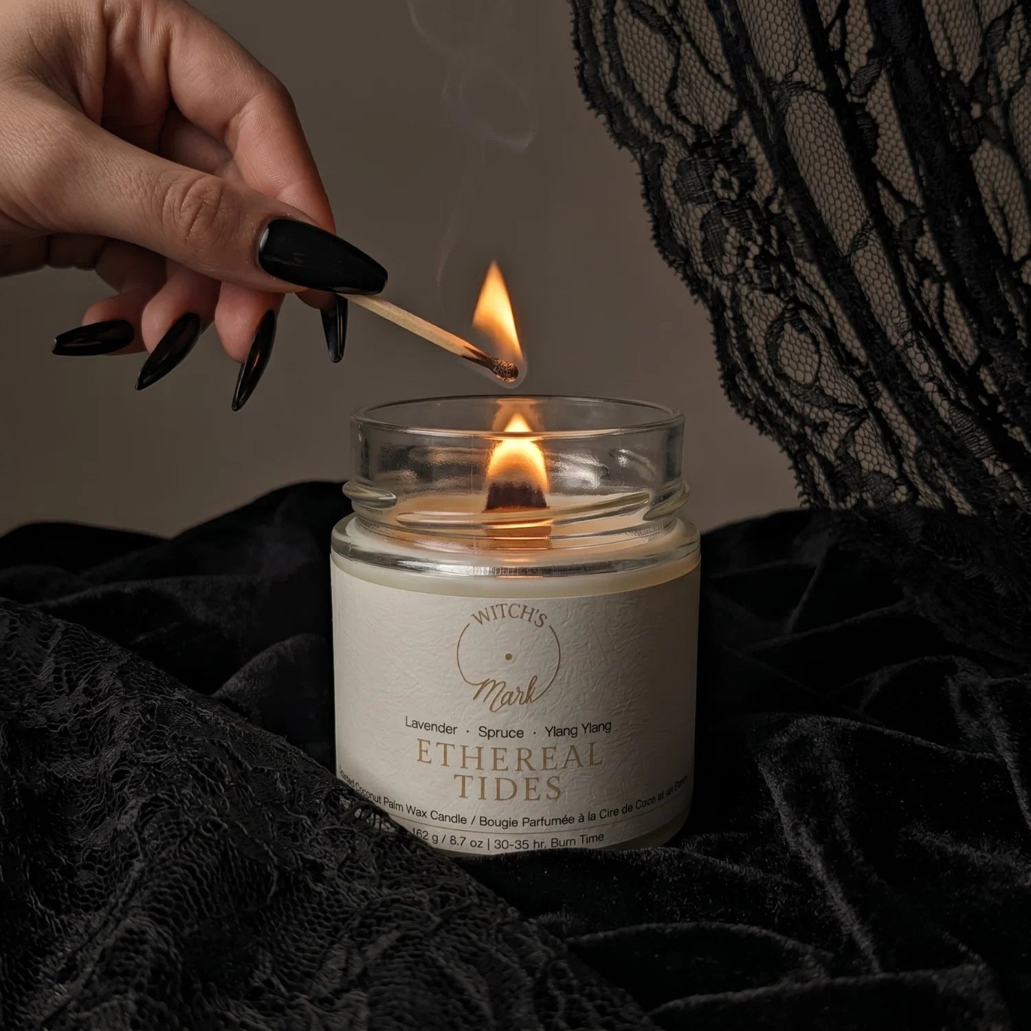 Hand lighting a candle labeled 'Ethereal Tides' with black lace in the background