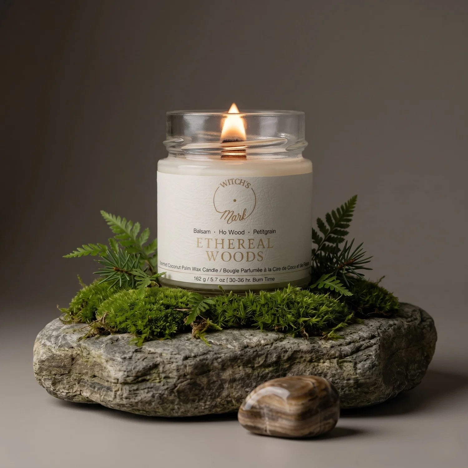 Ethereal Woods crystal candle on a rock surrounded with moss. In front of the candle and rock is a petrified wood crystal.