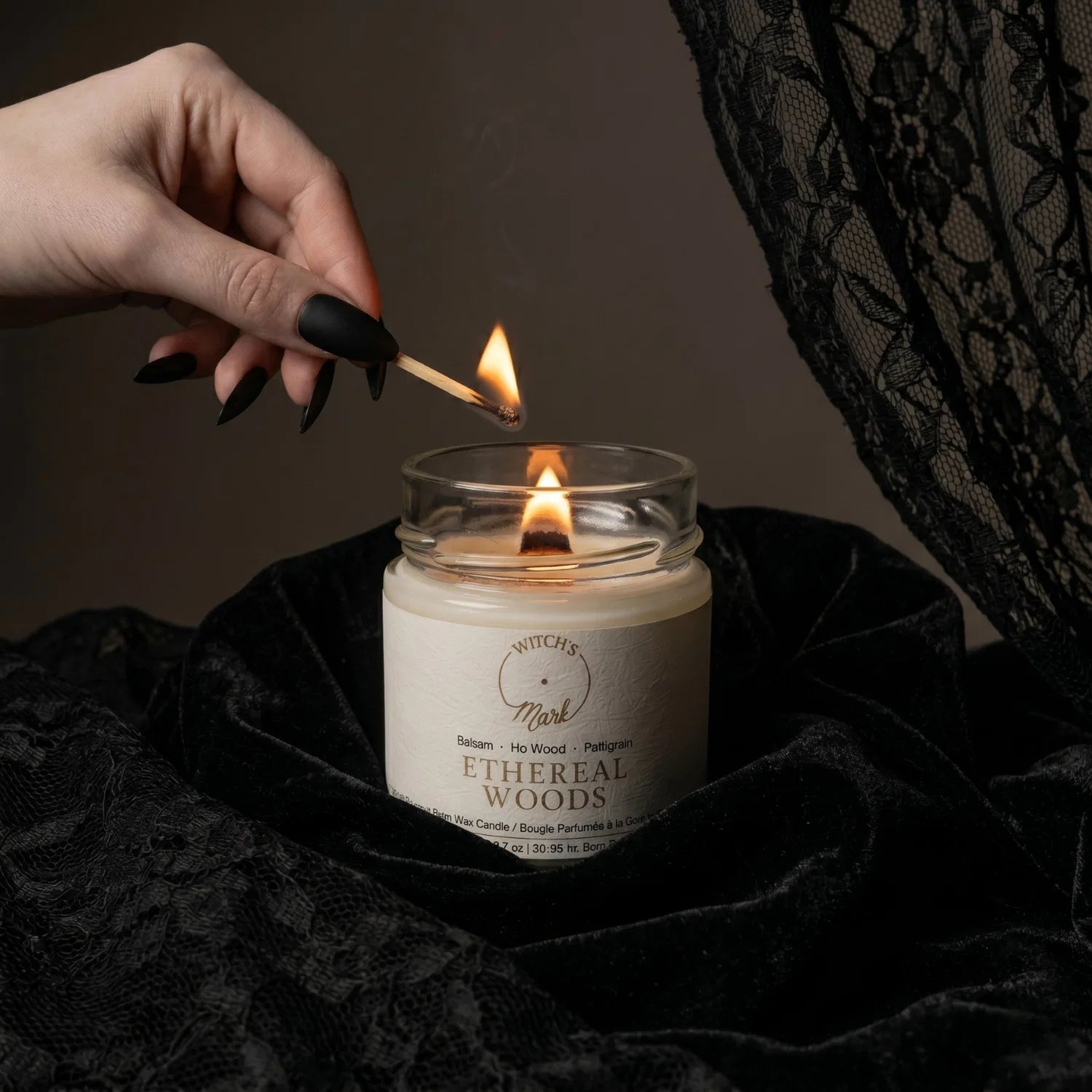 Hand lighting Ethereal Woods crystal candle in a moody room setting.