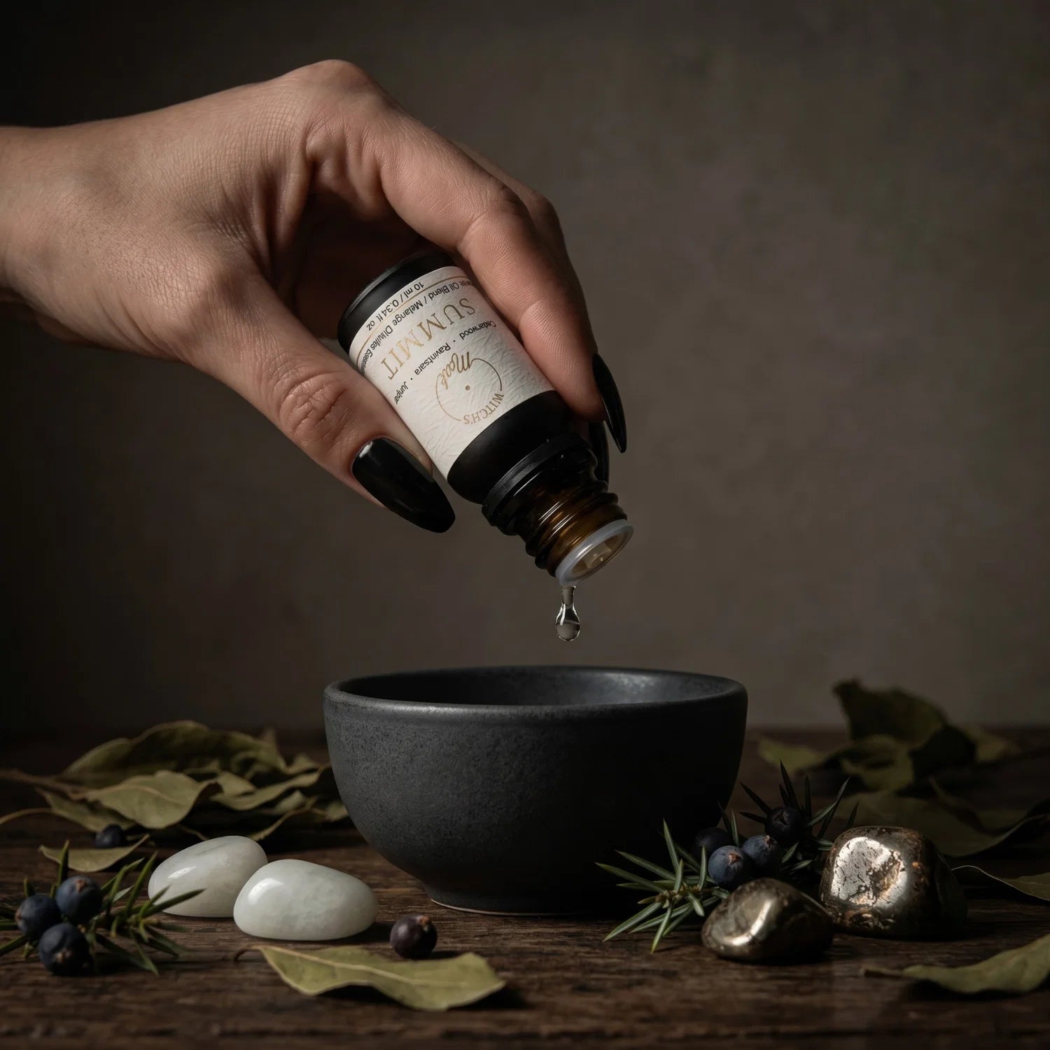Hand pouring oil from a essential oil bottle named Summit into a black bowl with a dark background. Next to the bowl is juniper and ravintsara leaves.