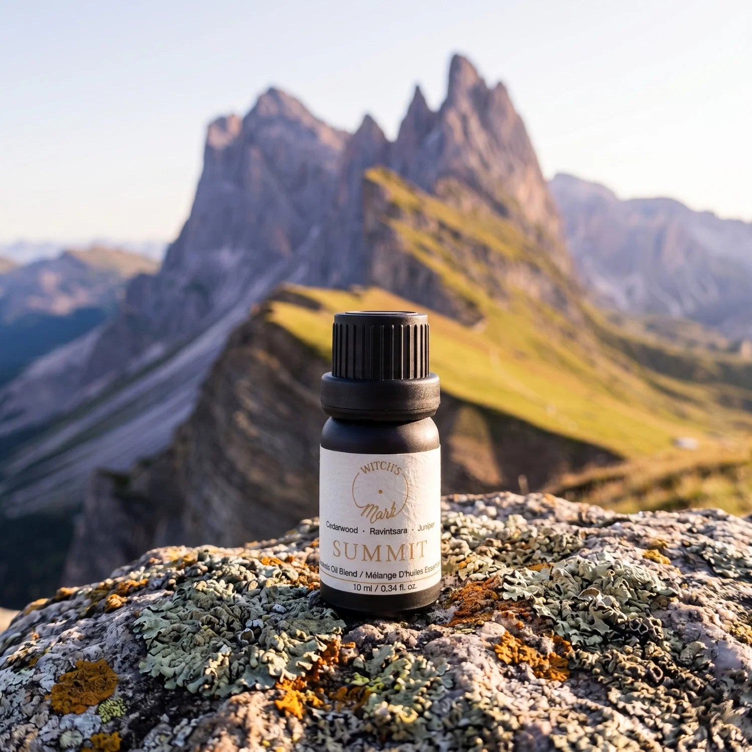 Summit essential oil bottle on a rocky mountain top with a mountainous background.