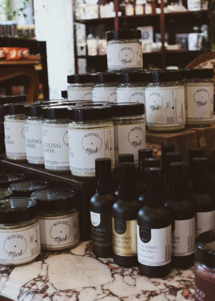 An indoor market display showcasing stacks of Witch's Mark crystal-infused candles and black ritual sprays at a local retail pop-up shop in Calgary.