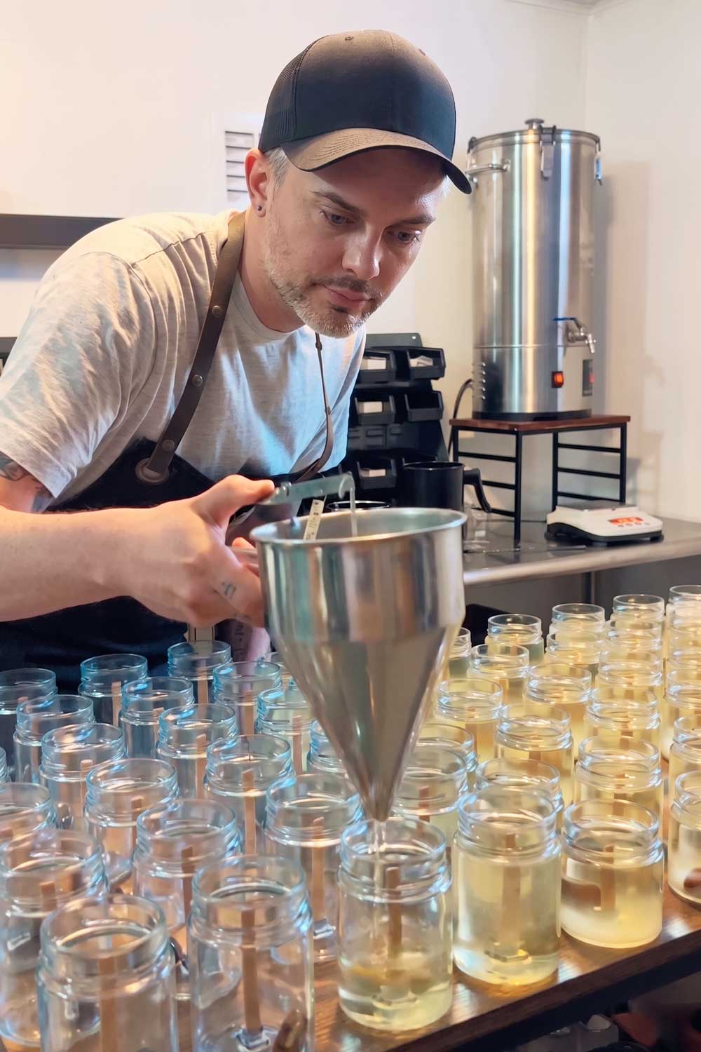 Person funneling wax into small glass containers in a candle making setting