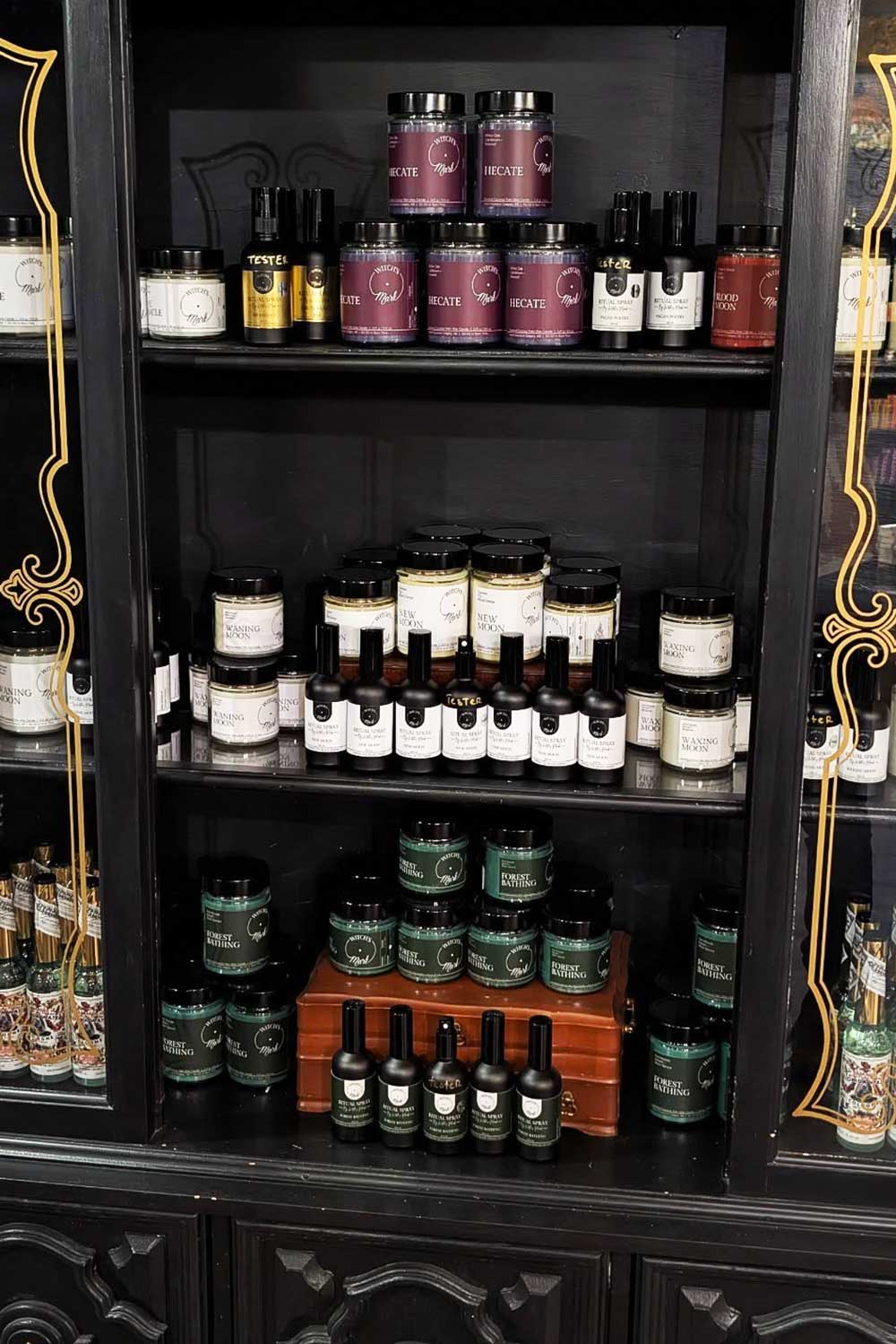 Shelving unit with Witch's Mark candles and ritual sprays in a decorative cabinet